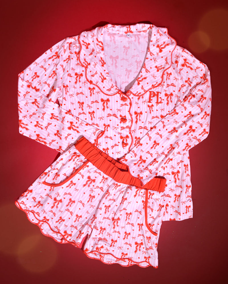 Bild av rosa och vit randig julpyjamas för vuxna med röd rosettdesign på en röd bakgrund