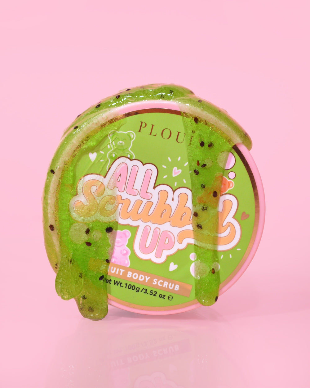 En behållare med P.Louise All Scrubbed Up Body Scrub med etiketten "Candy Bears" på en rosa bakgrund, där produkten ser ut som en grön gel
