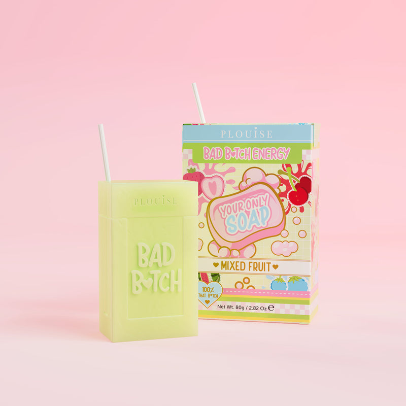 En grön tvål med 'Bad Bitch' ingraverad på den, åtföljd av en färgglad juicelåda med 'Mixed Fruit' märkt på, presenterad på en rosa bakgrund.