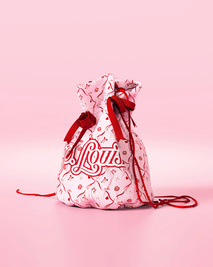 Rosa väska med dragsko med röda rosetter och en festlig design med "P.Louis"-märke på en rosa bakgrund