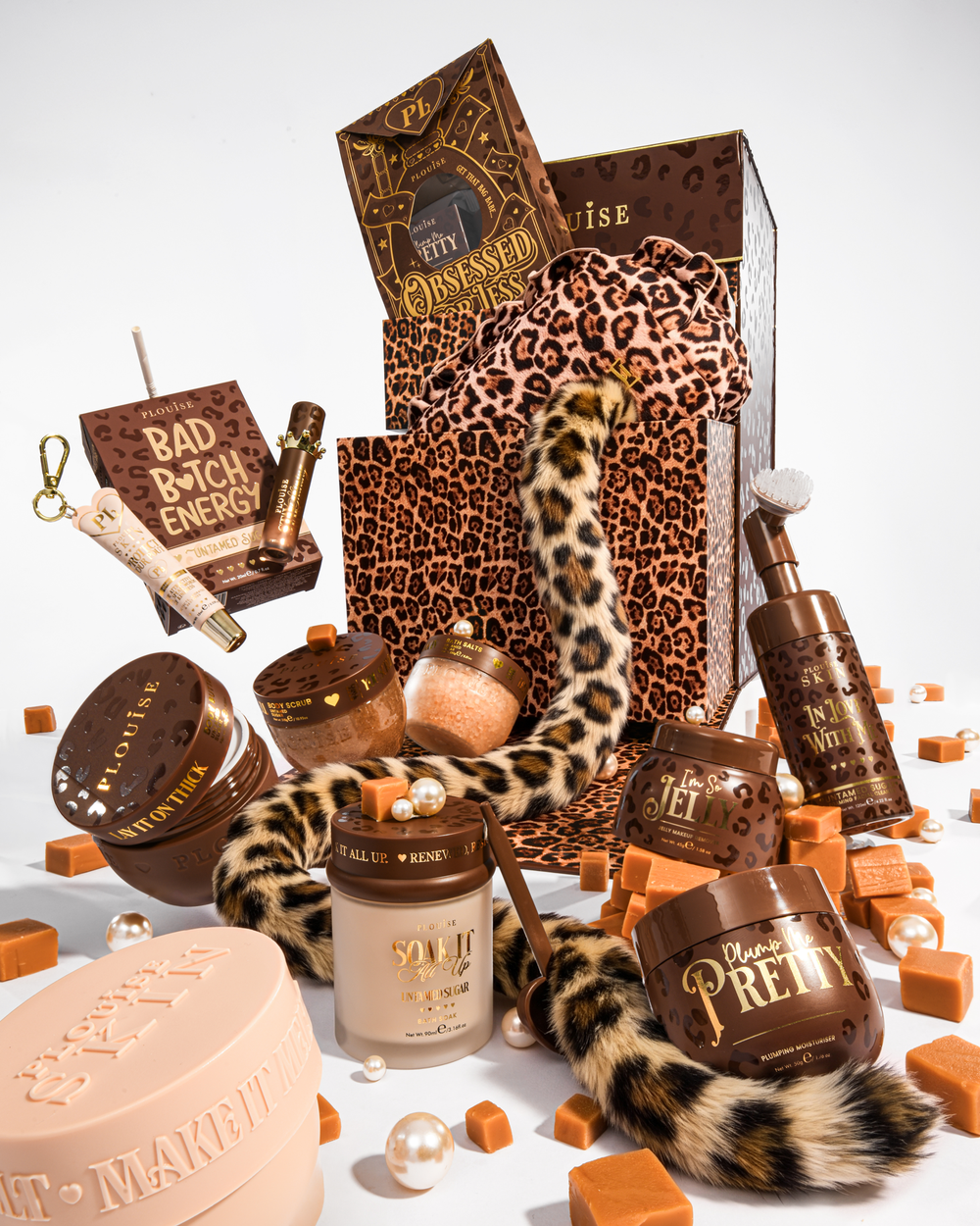 Ett lyxigt skönhetspresentset med bruna och leopardmönstrade element, inklusive en presentpåse med leopardmönstret, en svans med leopardmönstret och flera kosmetiska behållare i bruna och beige toner, arrangerade på en vit bakgrund med karamellfärgade kuber och pärlor.