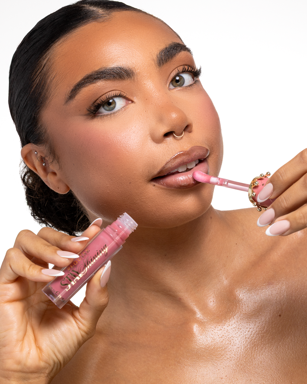 En närbild av en kvinna som applicerar en kvinna som applicerar en kvinna Sta piny Lips doe-fotsapplikator medan hon håller röret i sin andra hand, mot en ren vit bakgrund.