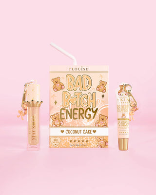 En P.Louise Teddy Glitter Bad Bitch Energy Lip Duo i doft av kokosnötskaka med läppbalsam och läppolja mot en rosa bakgrund