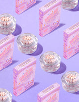 Klara behållare med P.Louise DOse of Dreams Vitamin C Capsule Face Cream med rosa kapsel i dem omgivna av rosa flingslådor på en lila bakgrund