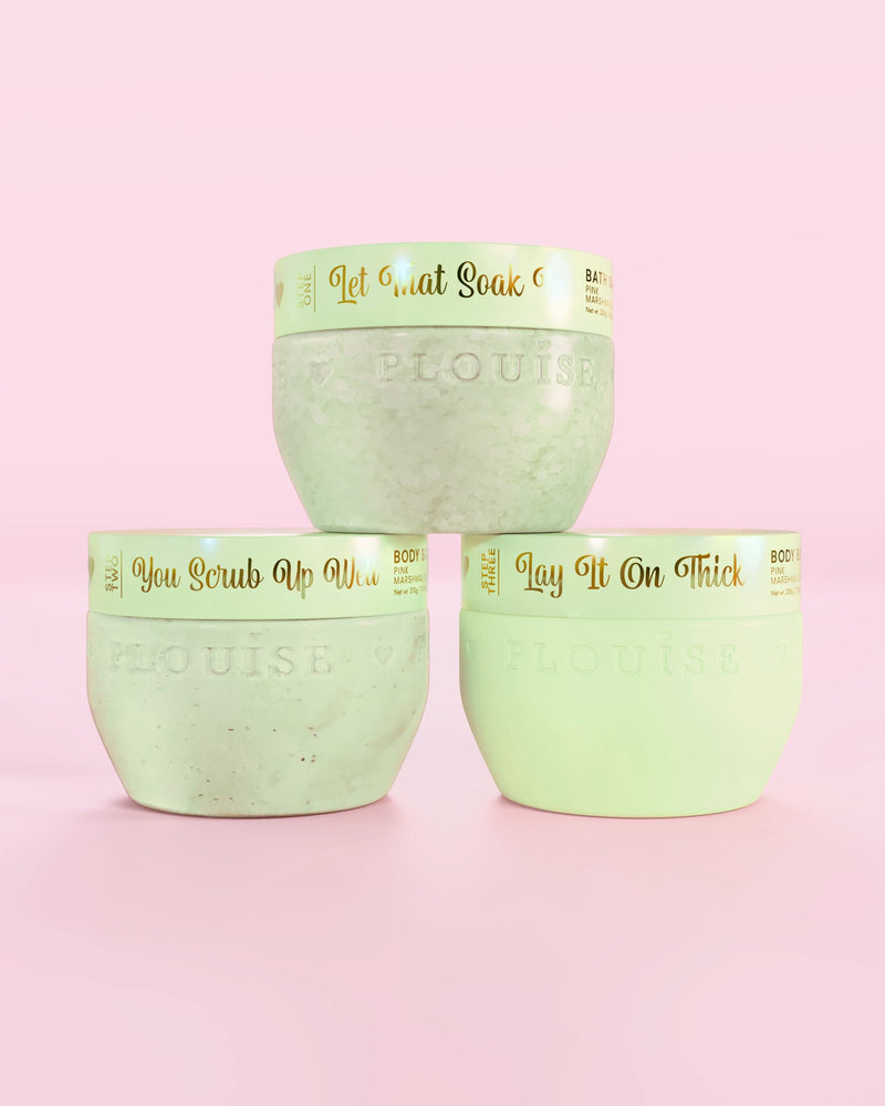 Tre P.Louise Hop Into Self-Care chokladtäckta jordgubbar gröna behållare med badsalt, kroppsskrubb och kroppssmör med guldtext på en rosa bakgrund