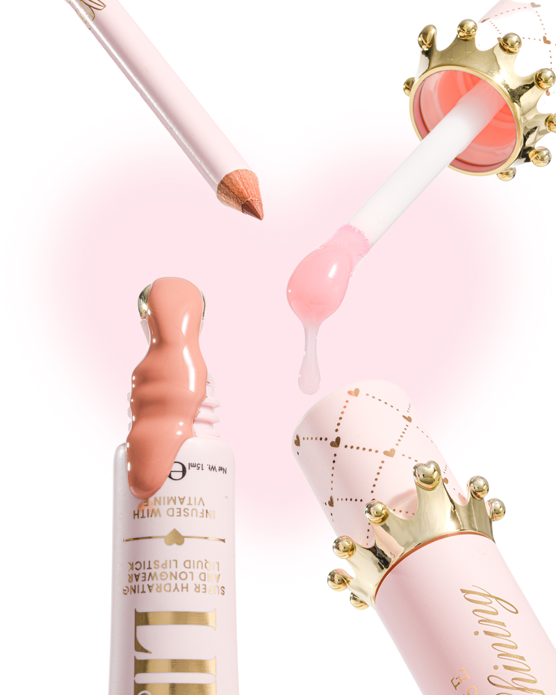 Pink and gold cosmetic product components arranged on a white background, including a lip base tube with peachy pink gloss, a doe-foot applicator with pink oil, a pink pencil, and a crown-decorated cap.