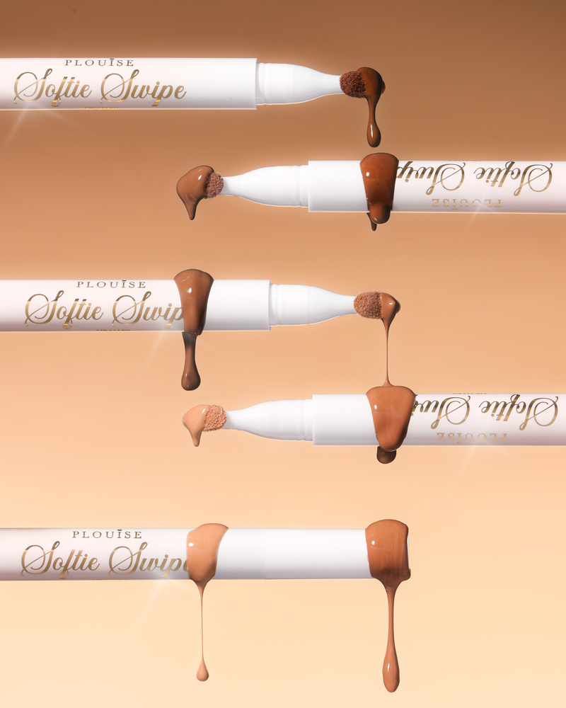 En bild av fem P.Louise Softie Swipe Tinted Lip Masks med produkt som droppar från spetsarna som visar de olika nyanserna mot en beige bakgrund