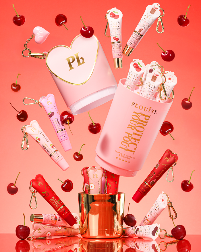 Pink XL Protect Your Pout Gift Set som öppnas omgiven av körsbär och rosa och röda läppbalsam på en rosa bakgrund