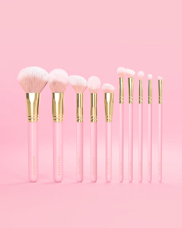Set med 10 rosa P.Louise sminkborstar med rosa handtag och gulddetaljer på en rosa bakgrund