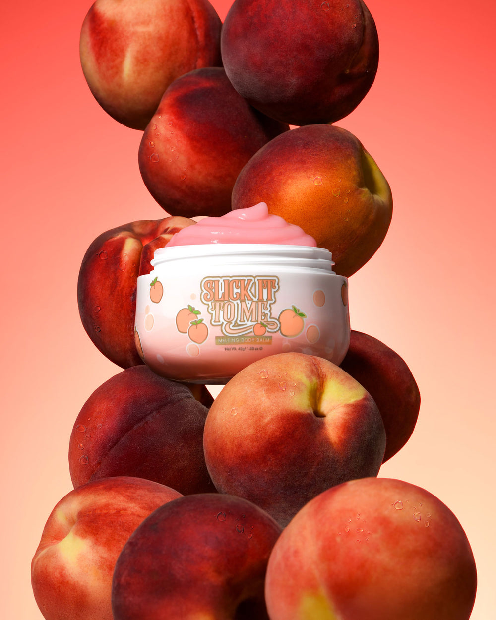 Burk med P. Louise Slick It To Me Peach Melting Body Balm med rosa kräm omgiven av persikor på en gradientbakgrund