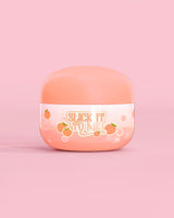 Burk med P. Louise Slick It To Me Peach Melting Body Balm med rosa bakgrund