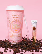 En produktbild med en ögonbrynspenna med dubbla ändar bredvid en tub med ögonbrynsgelé, uppsatt på en rosa yta med kaffebönor utspridda. Bakgrunden har en rosa kaffekopp med märkeselement.