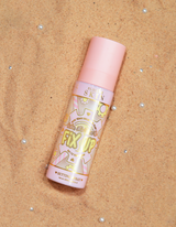 En flaska P.Louise Fix Up Mattifying Setting Spray med rosa lock och dekorativa mönster på etiketten, uppsatt på en sandig yta.