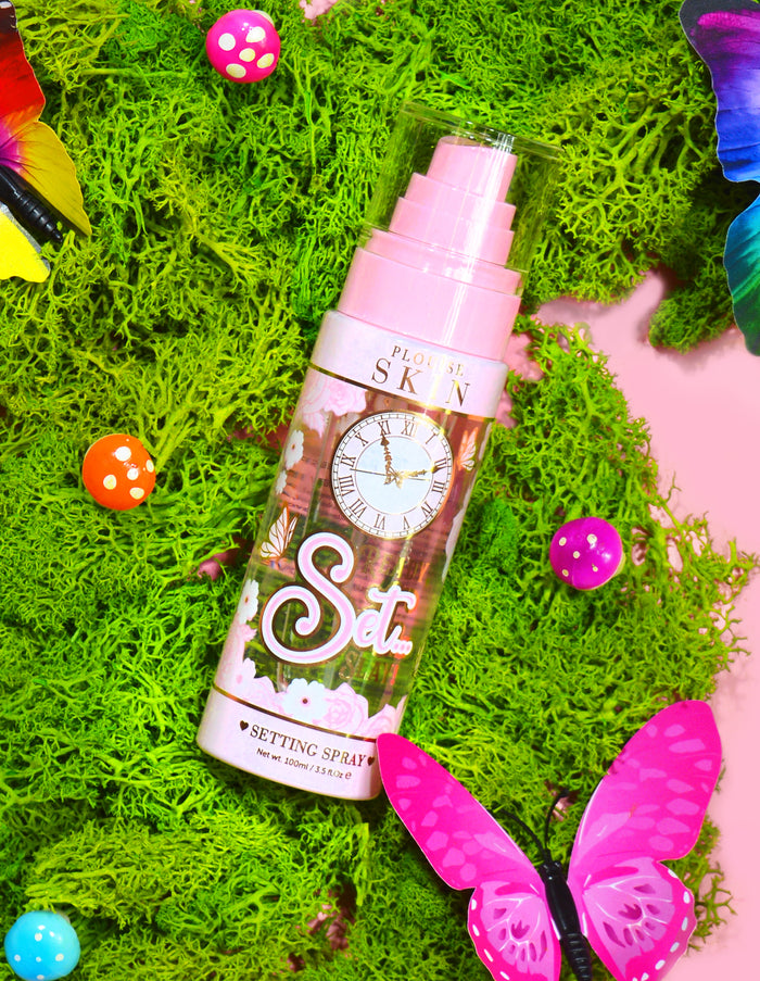 En flaska P. Louise Ready Set Slay Long Lasting Setting Spray omgiven av dekorativa element inklusive färgglad fuskmossa, fjärilar och svampar.