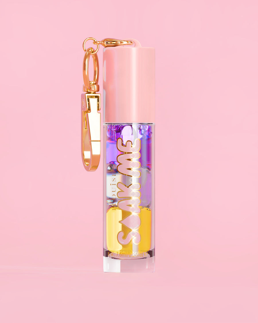P. Louise Soak Me Lip Oil med färgglad lagerolja i en rosa tub med ett guldlås på en rosa bakgrund