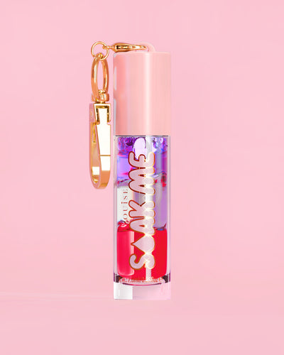 P. Louise Soak Me Lip Oil med färgglad lagerolja i en rosa tub med ett guldlås på en rosa bakgrund
