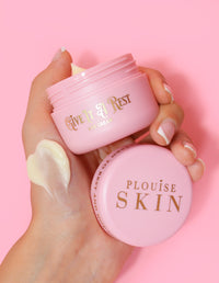 En person som håller i en rosa burk med P.Louise Give It A Rest ögonkräm med locket av, med produktnamn och märke på burken.