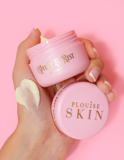 En person som håller i en rosa burk med P.Louise Give It A Rest ögonkräm med locket av, med produktnamn och märke på burken.